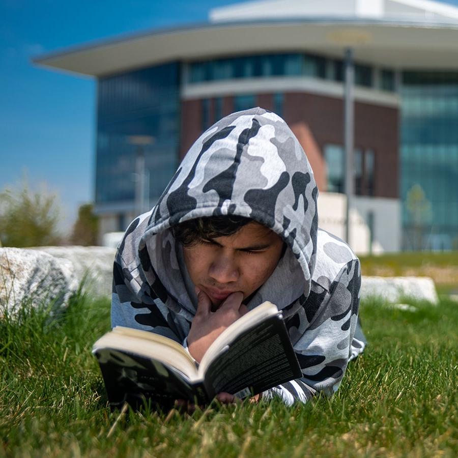 student lying on campus lawn reading a book